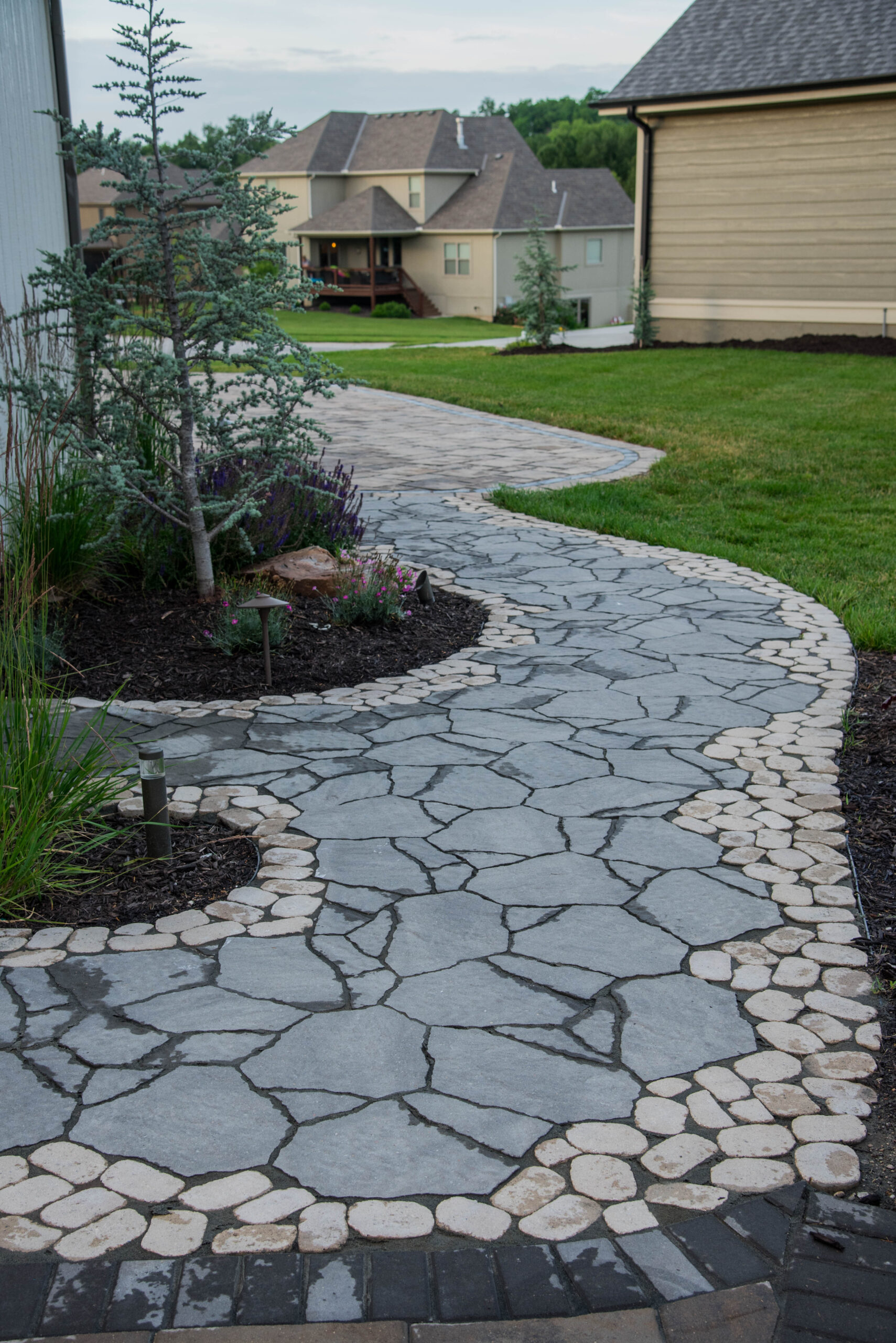 Curved stone pathway with natural landscaping, featuring greenery and flowers, showcasing quality hardscaping by Atlas Landscape.
