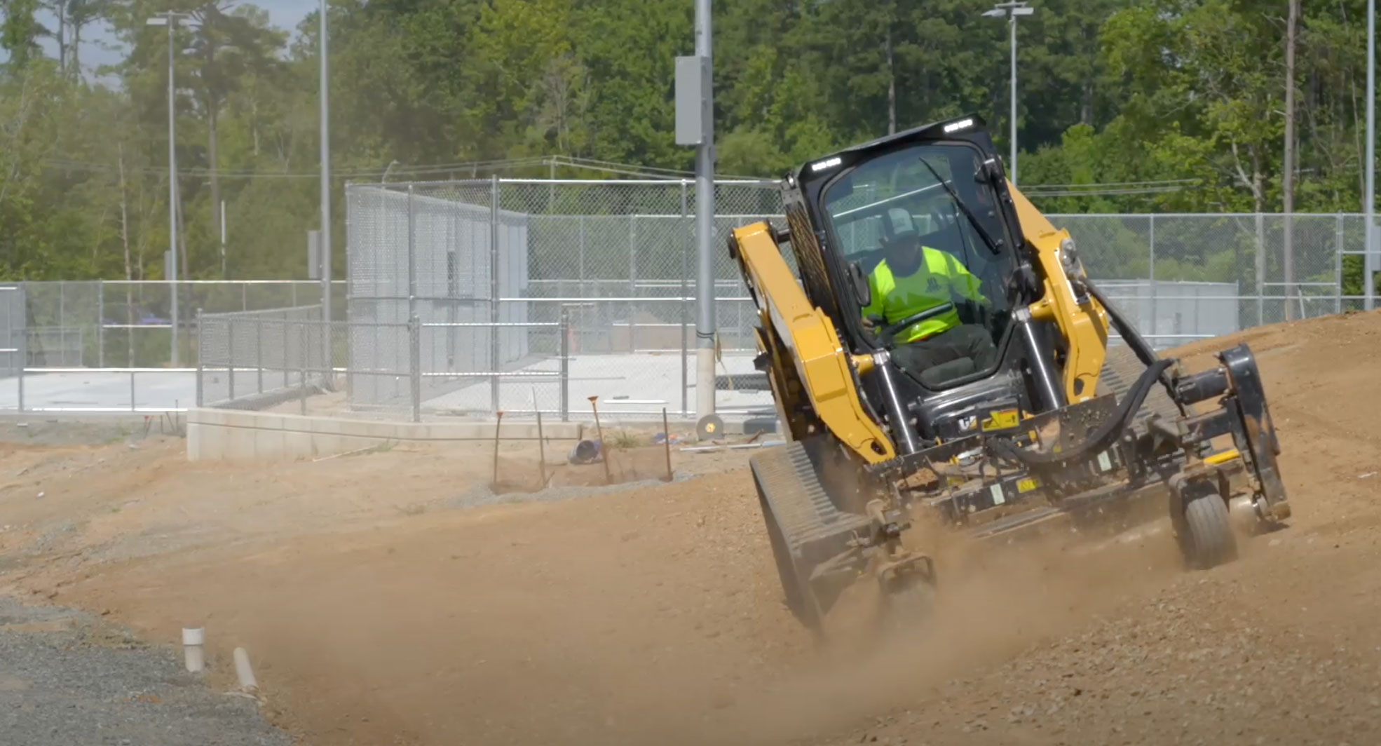 Heavy machinery operating on a construction site, focused on land management and site preparation, with a worker in a safety vest directing the equipment amidst dust and gravel.